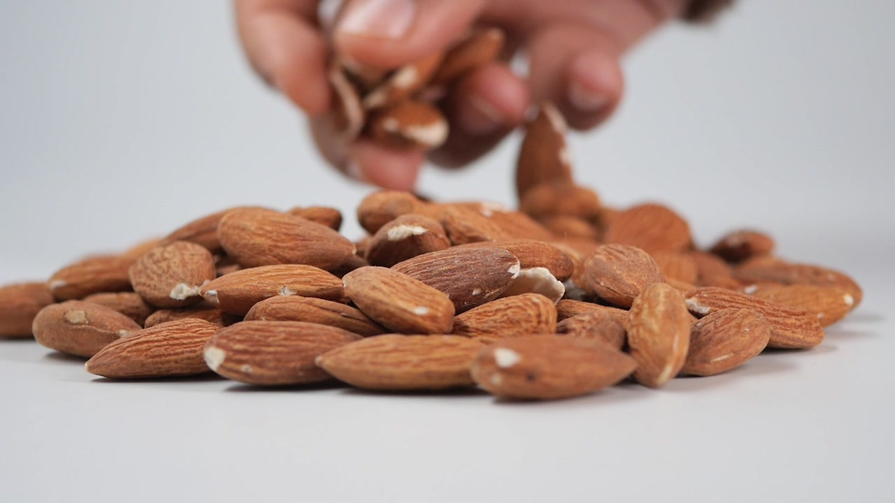Hand Picking Up Almonds from a Pile on a White Background