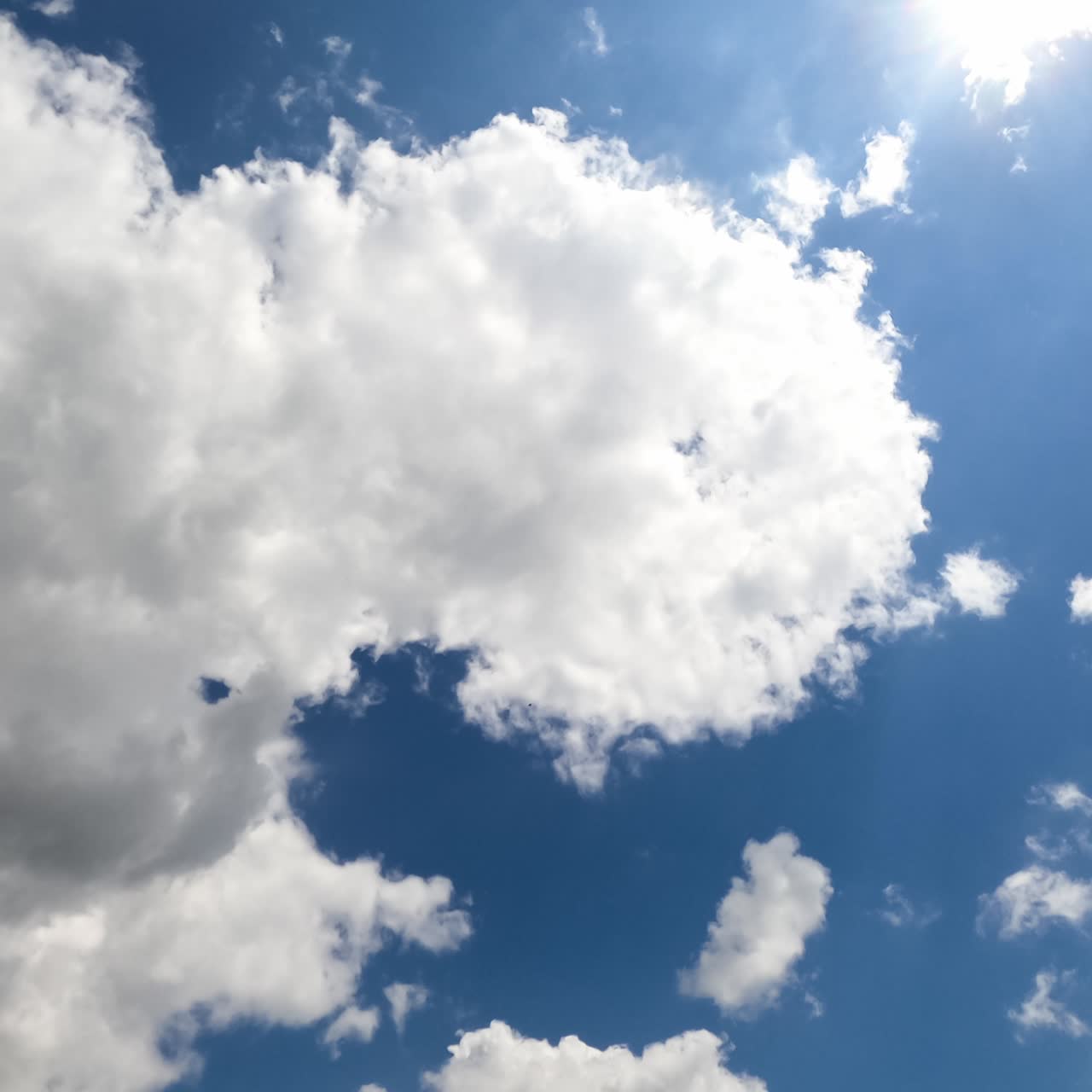 White puffy clouds flying through against the shining sun. Cumulus clouds gathering into a grey cloudscape timelapse. View from below