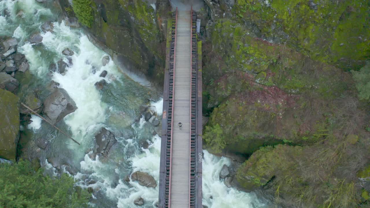 toma aérea de drones de una persona en un puente colgante sobre el río creek entrando en una cueva, ubicada en el parque provincial del cañón coquihalla del túnel othello en columbia británica bc canadá