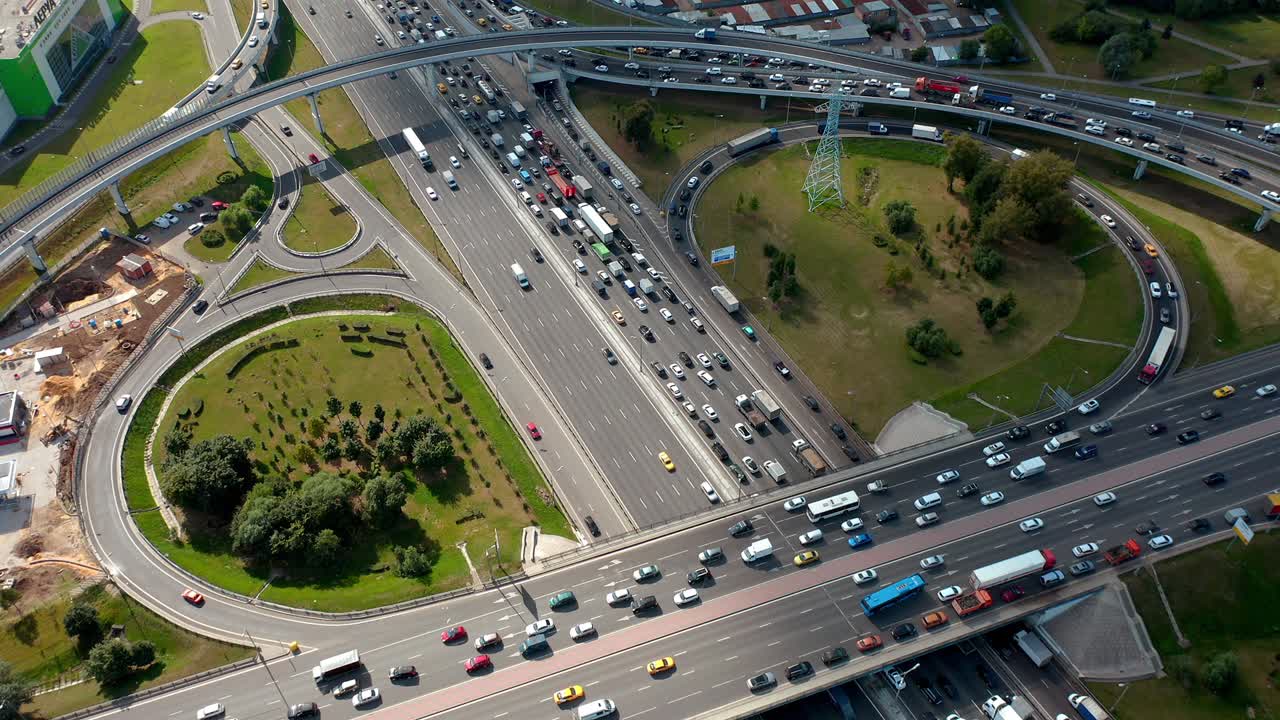gran intersección con salidas de trébol y tráfico pesado de cerca. bajo la sombra de las nubes. vista aérea superior de avión no tripulado. muchos coches en la rutina de tráfico cotidiano. áreas de plantación verde a su alrededor. la cámara se mueve hacia adelante sobre la carretera y mirando hacia abajo..