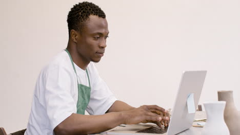 american clerk in apron sitting in front of laptop and typing on keyboard