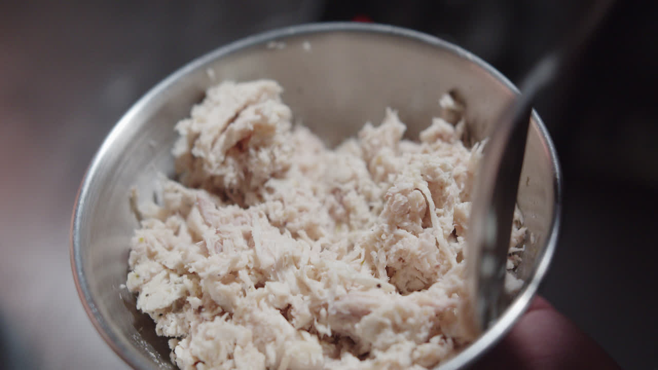 Amazing slow motion shot of a bowl of shredded chicken as a professional chef moves and mixes it with a spoon and then serves it on a Mexican tortilla
