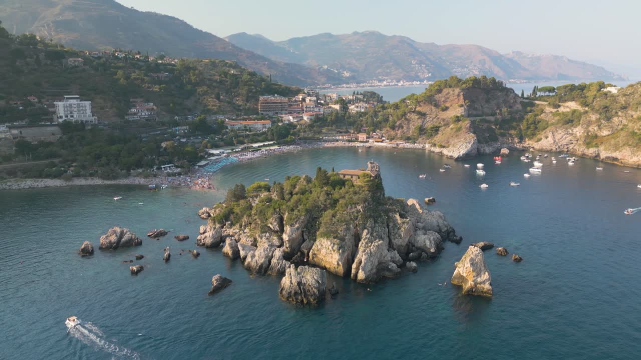 Ripresa aerea in allontanamento che rivela la splendida Isola Bella a Taormina, meta turistica siciliana.