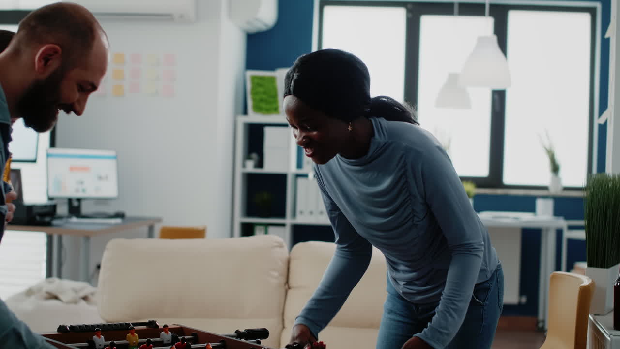 Multi ethnic coworkers playing soccer game at foosball table