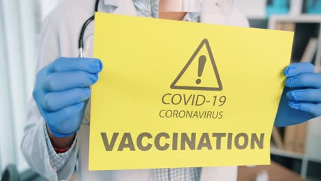 Nahaufnahme-Von-Personenhänden-In-Schutzhandschuhen,-Die-Eine-Papierkarte-Mit-Ankündigung-über-Coronavirus-Impfkampagne,-Covid-19-Impfstoff,-Aufmerksamkeit,-Gesundheitsbenachrichtigung-Halten