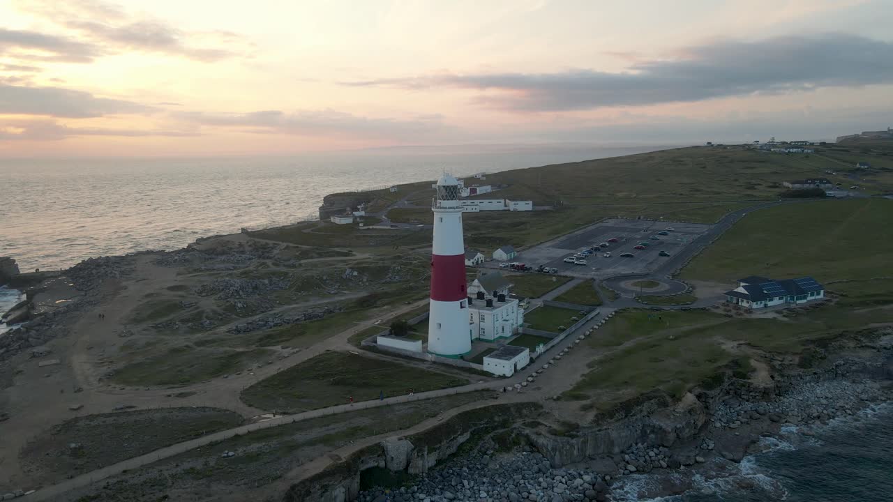 drone viajando hacia atrás desde el faro de portland bill, una isla en dorset, inglaterra, con una hermosa puesta de sol en el fondo