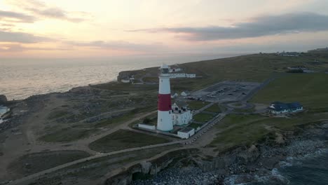 Drone-travelling-backwards-from-Portland-Bill's-lighthouse,-an-island-in-Dorset,-England,-with-a-beautiful-sunset-in-the-background