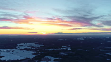 toma en ángulo alto sobre el paisaje invernal con bosque cubierto de nieve a lo largo de la carretera con un cielo amarillo brillante al amanecer sobre el horizonte