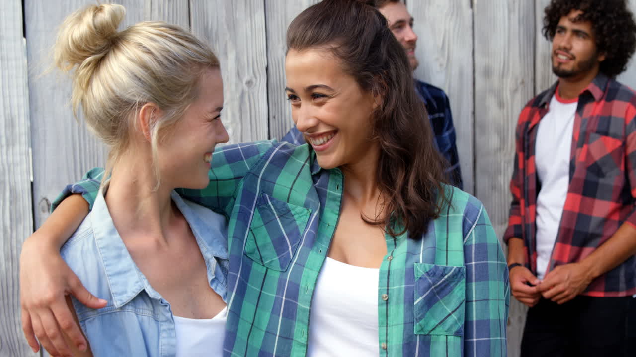 mujeres jóvenes con brazos alrededor mientras los hombres interactúan en el fondo