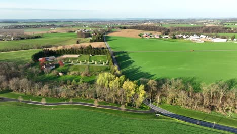 Aerial-wide-shot-showing-green-agricultural-fields-of-american-and-rural-main-road-at-sunset