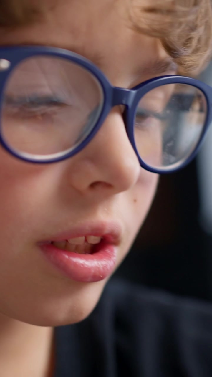 Giovane ragazzo concentrato con gli occhiali che scrive su carta con una penna