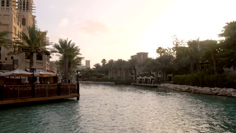 landscape with canal, tropical palms and traditional arabic buildings with cafe in evening