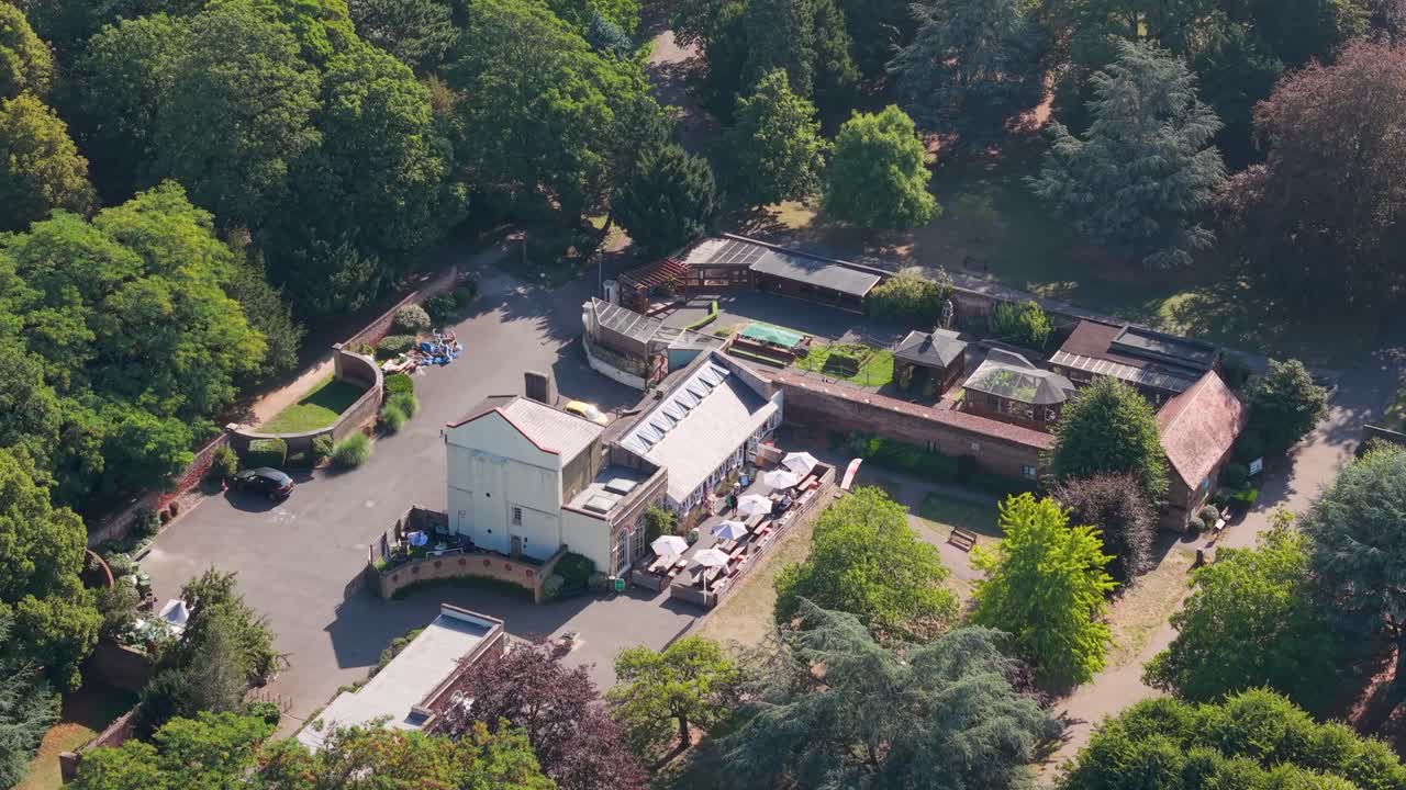 Drone flyover at 45 degrees over Cedar’s Park, Cheshunt, England, passing near green summer trees and historic buildings