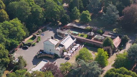 drone flyover at 45 degrees over cedar’s park, cheshunt, england, passing near green summer trees and historic buildings