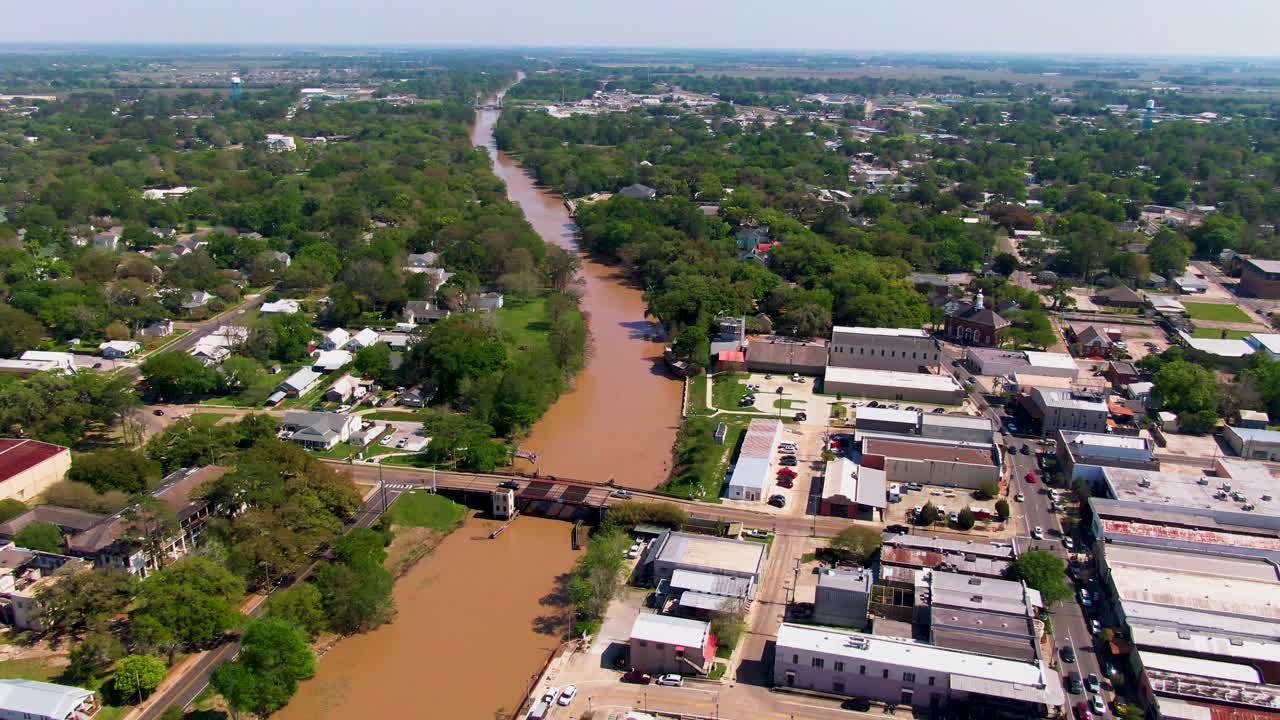 Drone shot zooming out over Bayou Teche and downtown New Iberia, LA, revealing the Duperier Bridge, parking lots, and the surrounding cityscape