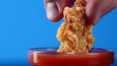 chicken strips dipped in a bowl with tomato sauce.