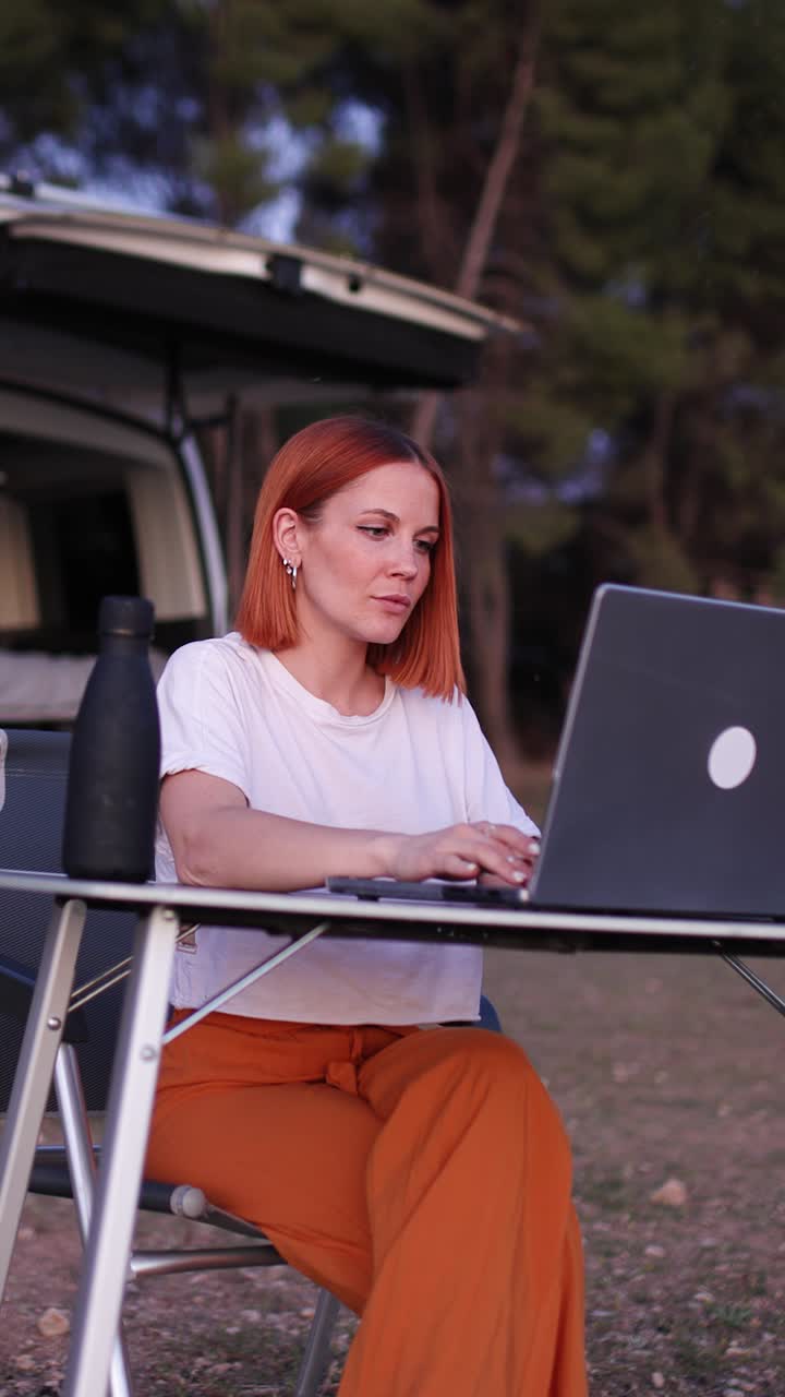 Giovane donna che lavora al laptop all'aperto in campeggio