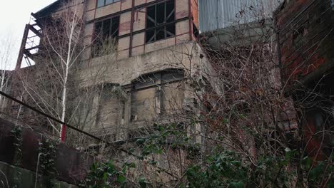 an abandoned, dilapidated multi-storey building with broken windows and crumbling walls, overgrown with vegetation