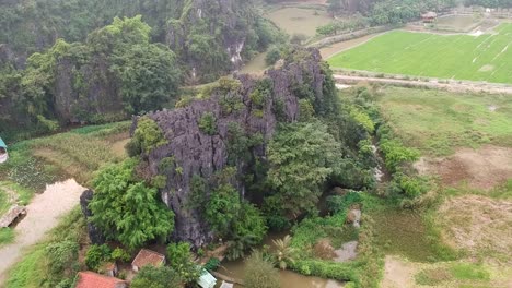 Aerial-ascend-over-giant-limestone-rock-in-Vietnamese-countryside-of-Tam-Coc,-Ninh-Binh,-Vietnam