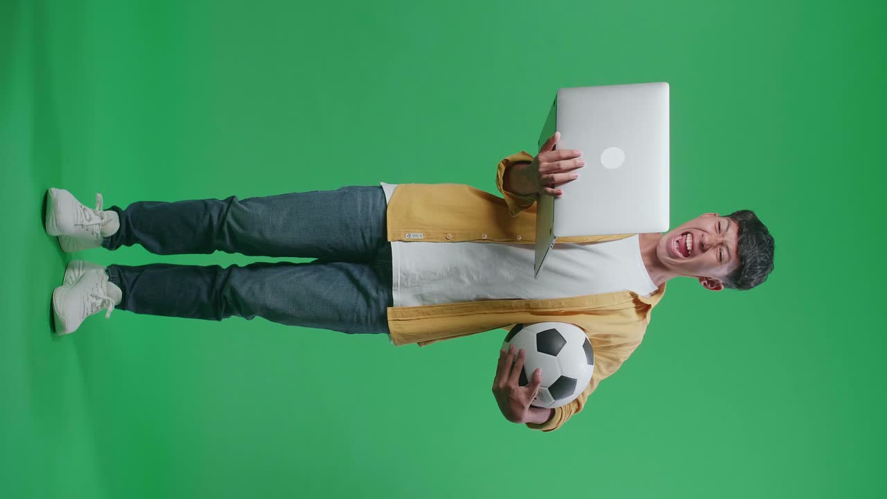 cuerpo lleno de niño asiático con una pelota está gritando meta estar feliz por el equipo ganador mientras aplaude el fútbol en una computadora portátil en el estudio de pantalla verde