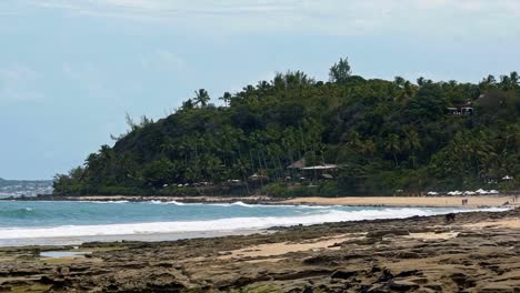 Slow-motion-shot-of-waves-crashing-into-rocks-on-the-beautiful-tropical-Tibau-do-Sul-beach-in-Rio-Grande-do-Norte,-Brazil-covered-in-golden-sand,-palm-trees,-and-cliffs-of-exotic-plants-a-summer-day