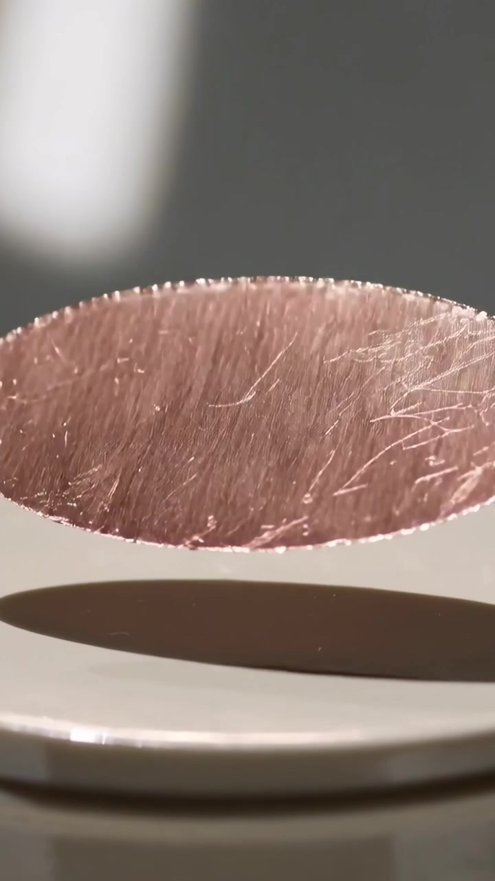 Video verticale: Disco di rame inclinato che scende al rilascio in studio su un piatto bianco riflettente