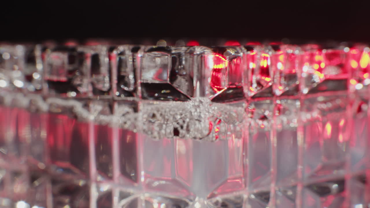 Close-up of a crystal glass with red light reflections and bubbles