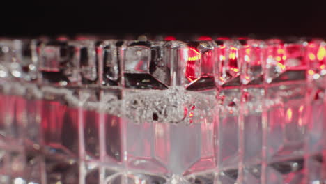 close-up of a crystal glass with red light reflections and bubbles