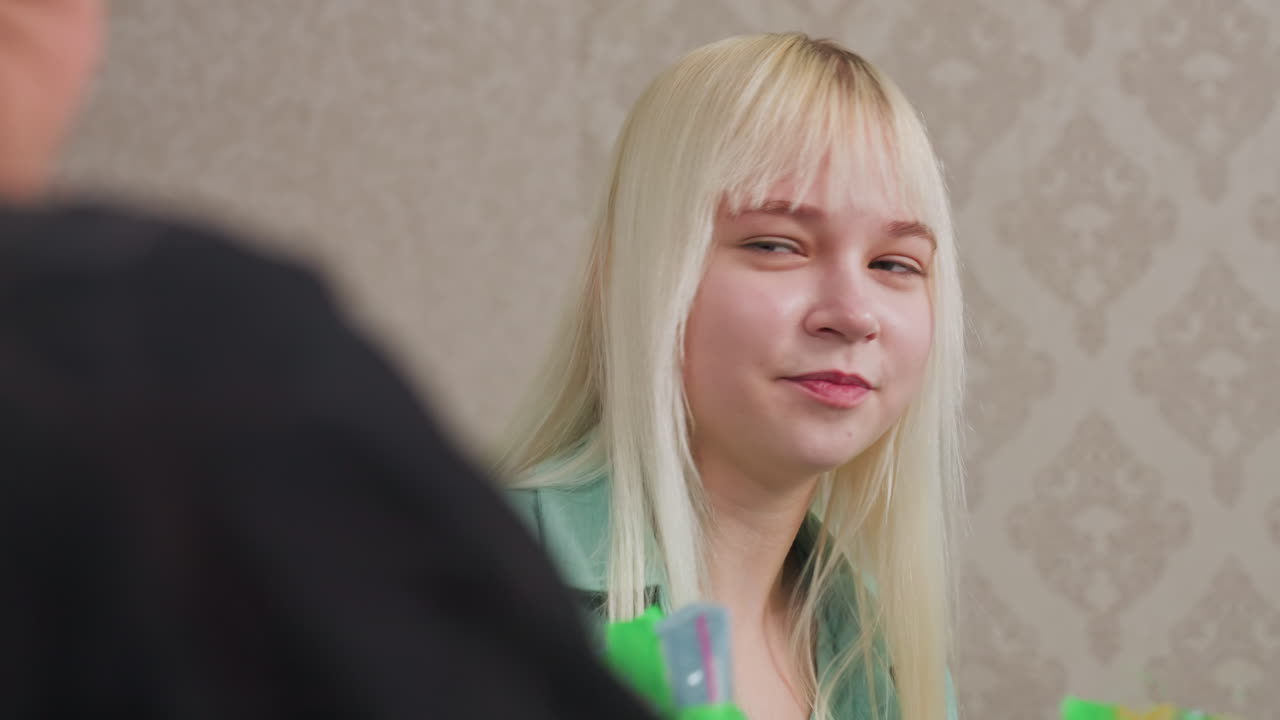 close up of two friends happily interacting while holding green candy pack, indoor setting with cheerful mood, candid moment of enjoyment and friendship sharing snacks