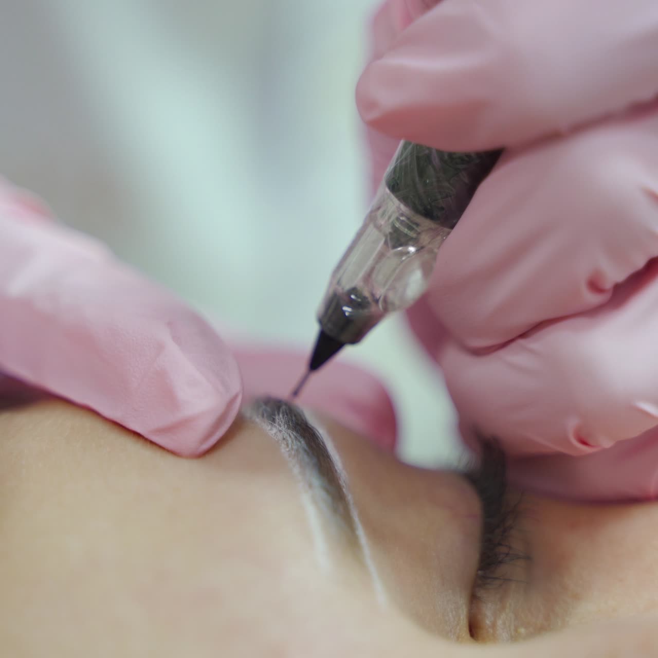 master is making permanent make-up of eyebrows with professional needle. Eyebrows shape correction. Cosmetology