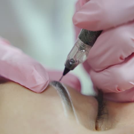 master is making permanent make-up of eyebrows with professional needle. eyebrows shape correction. cosmetology