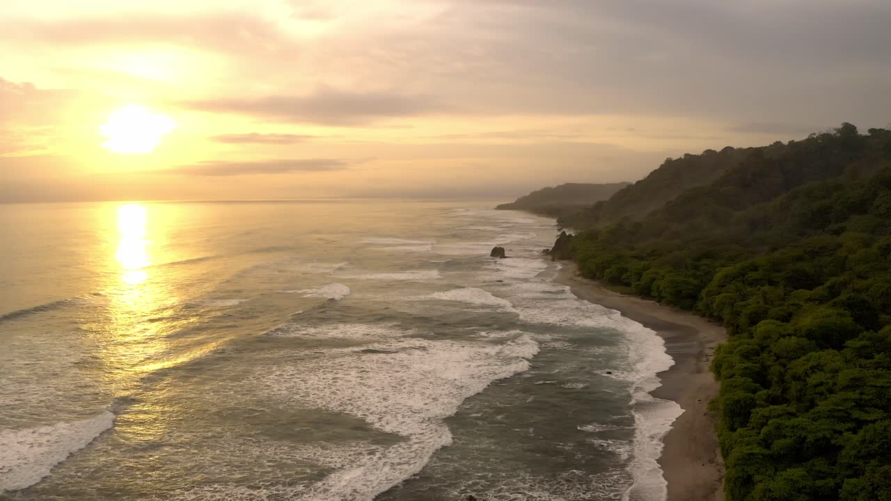 Una vista aerea cattura il tramonto tranquillo sulla costa di Santa Teresa in Costa Rica, con onde che si infrangono lungo una spiaggia sabbiosa incorniciata da lussureggianti colline verdi