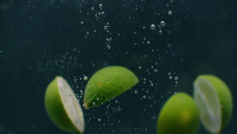 green limes are thrown into a container of water. video of fruit in slow motion