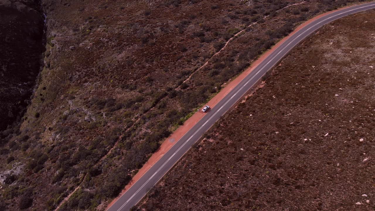 Drone shot shows a two way high way road, whilst one of the vehicles parks on the side of the road and others passing by driving.
