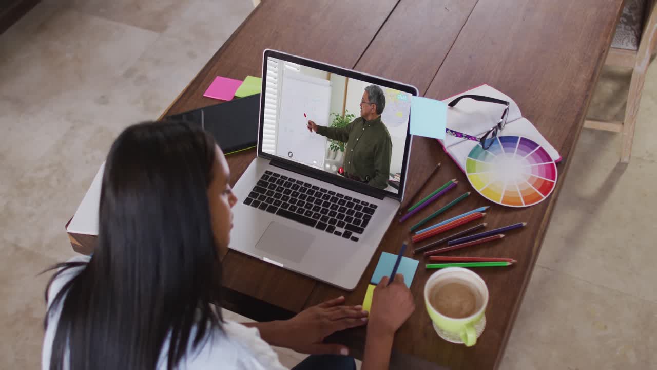 estudiante caucásica usando una computadora portátil en una videollamada con un profesor masculino, tomando notas