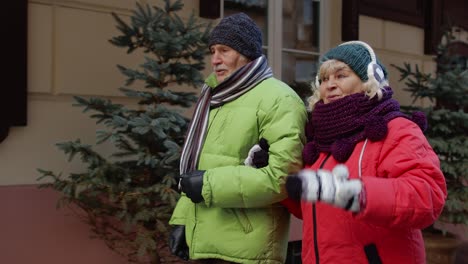 pareja feliz de turistas ancianos hombre y mujer caminando, hablando, gesticulando en invierno ciudad europea nevada