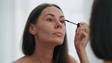 confident woman applying mascara mirror place. beautiful model preparing makeup