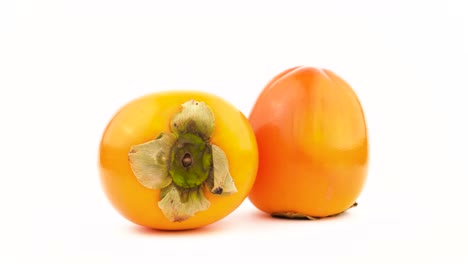 two persimmon kaki fruits. rotating on the turntable. isolated on the white background. close-up. macro.