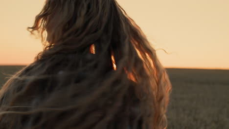 teenage girl with long hair quickly rotates her head at sunset, plays with her hair