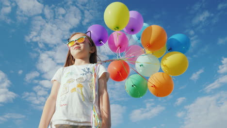 A-Cheerful-Girl-With-Balloons-Is-Standing-On-A-Green-Meadow-Enjoy-The-Warmth-And-Fly-Of-The-Concept