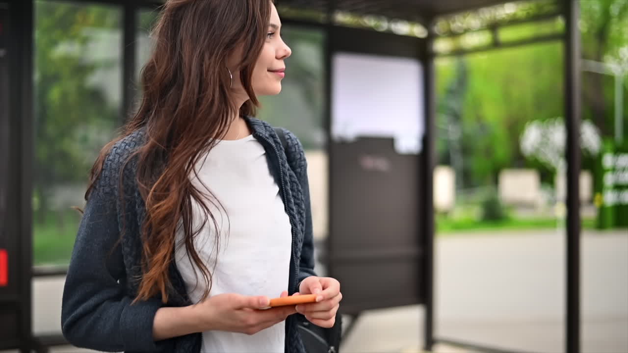 Donna con smartphone che cammina alla fermata del filobus, altre persone sullo sfondo. Movimento rallentato