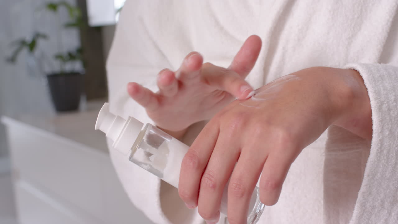 Applying lotion, woman in white robe taking care of skin at home spa