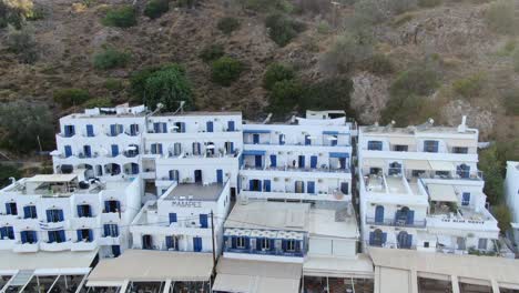 drone view in greece flying in front of white houses next to a brown hill on the mediterranean on a sunny day