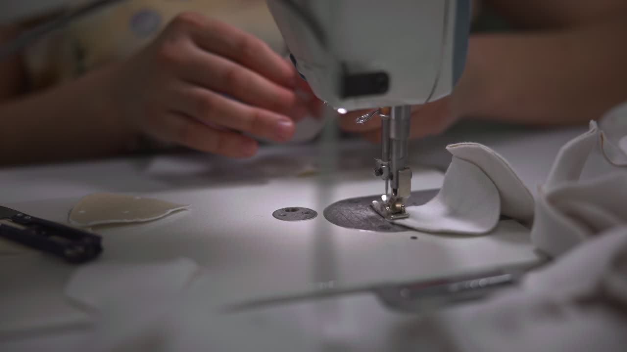 Primer Plano de Máquina de Coser con Manos Guiando Tela Blanca Debajo del Prensatelas, Formación Cuidadosa de la Puntada