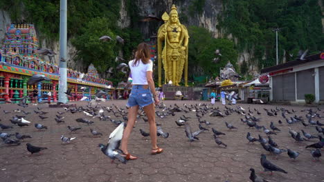 toma en cámara lenta de una mujer girando y caminando entre un grupo de palomas hacia las cuevas de batu en selangor, malasia