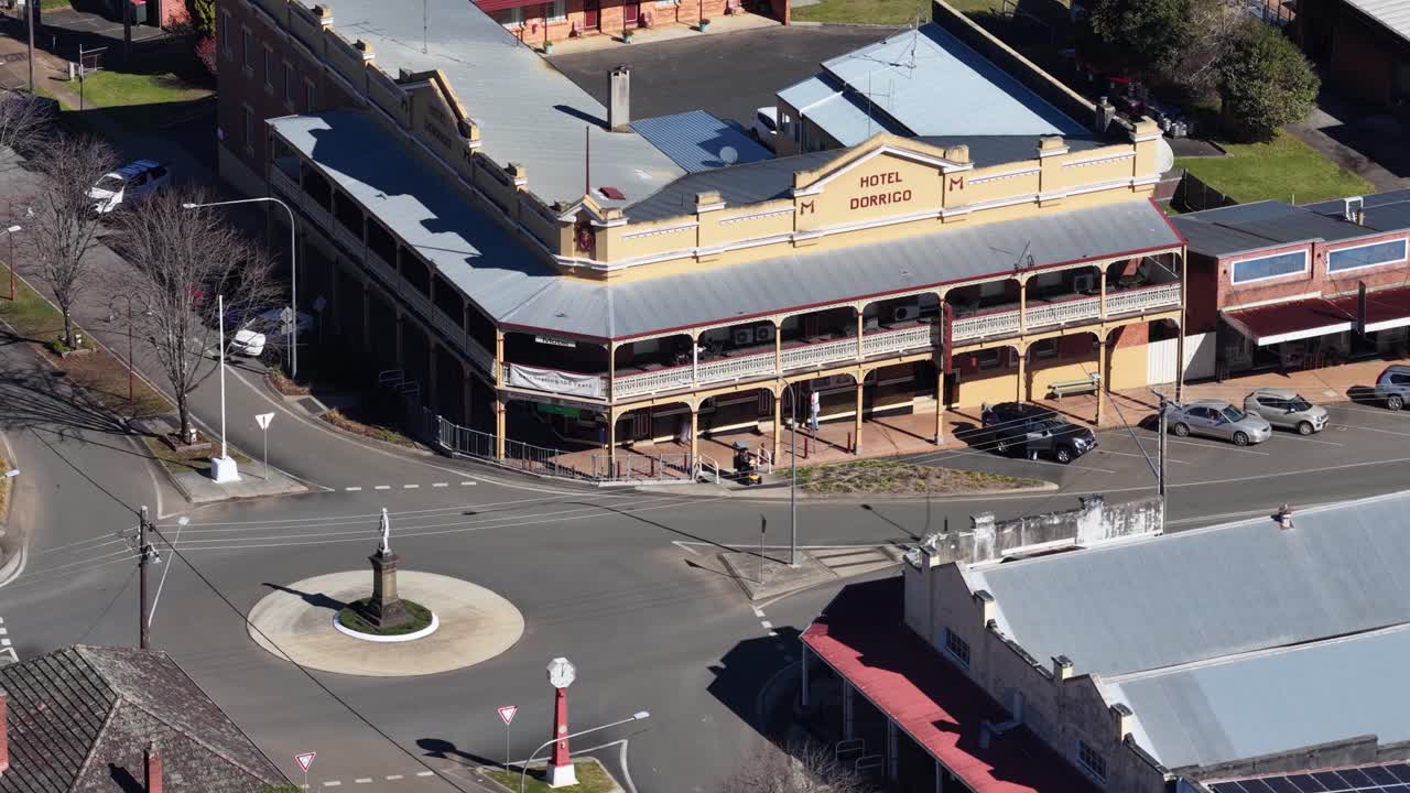 Drone ascends above Dorrigo roundabout, revealing heritage buildings, cars, and sunlit streetscape