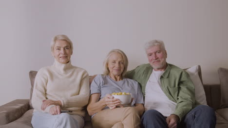 portrait of three senior people sitting on sofa and smiling at camera