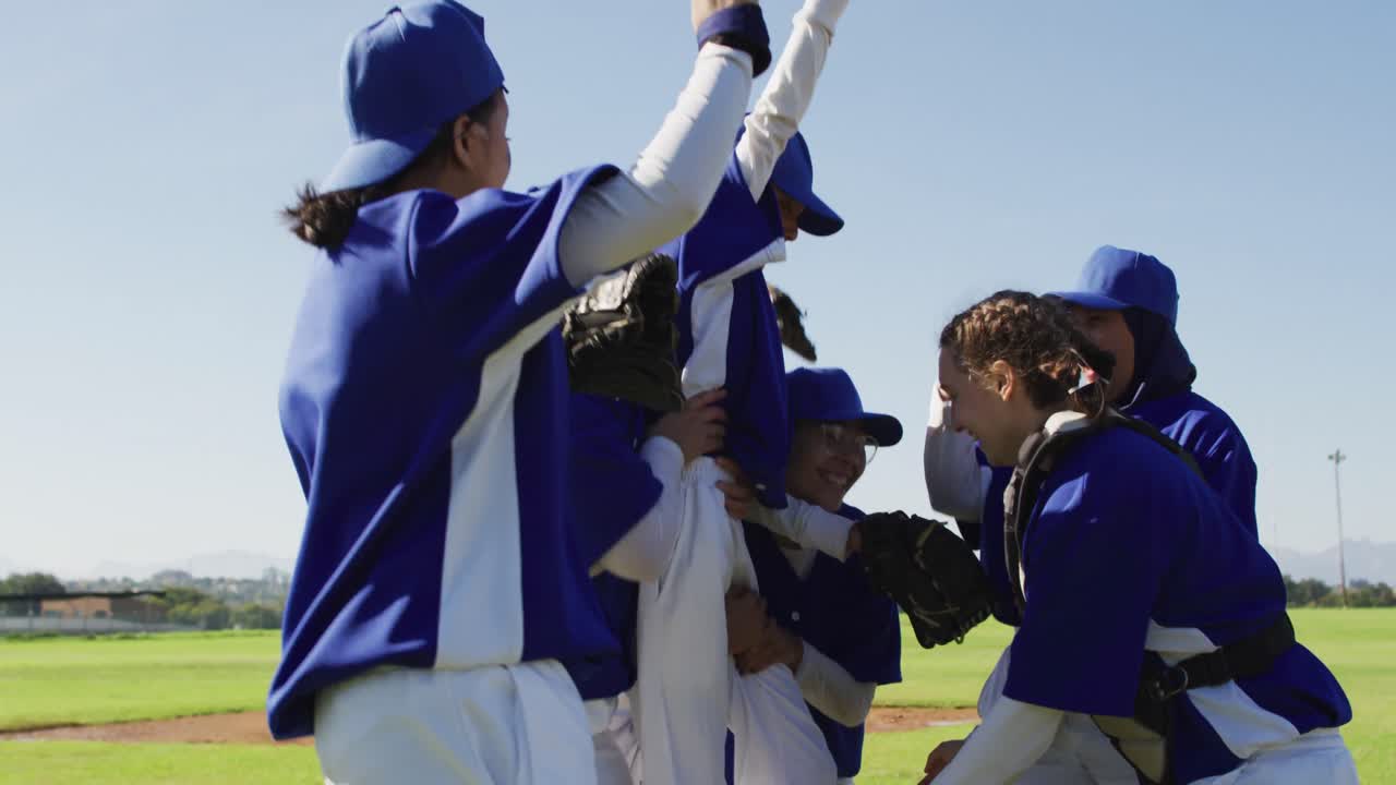feliz equipo diverso de jugadoras de béisbol celebrando después del juego, levantando a una jugadora