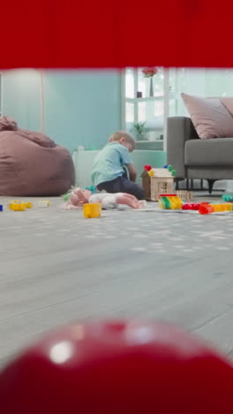 toddler builds house from blocks sitting on wooden floor. little boy enjoys weekend at home view through clearance in construction of cubes