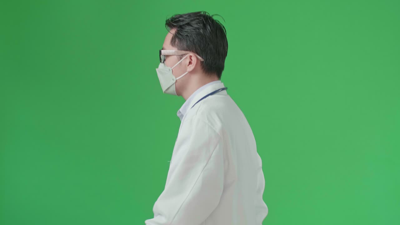 The Side View Of Asian Doctor With Stethoscope Wearing Mask, Glasses, And White Coat Walking On Green Screen Chroma Key.